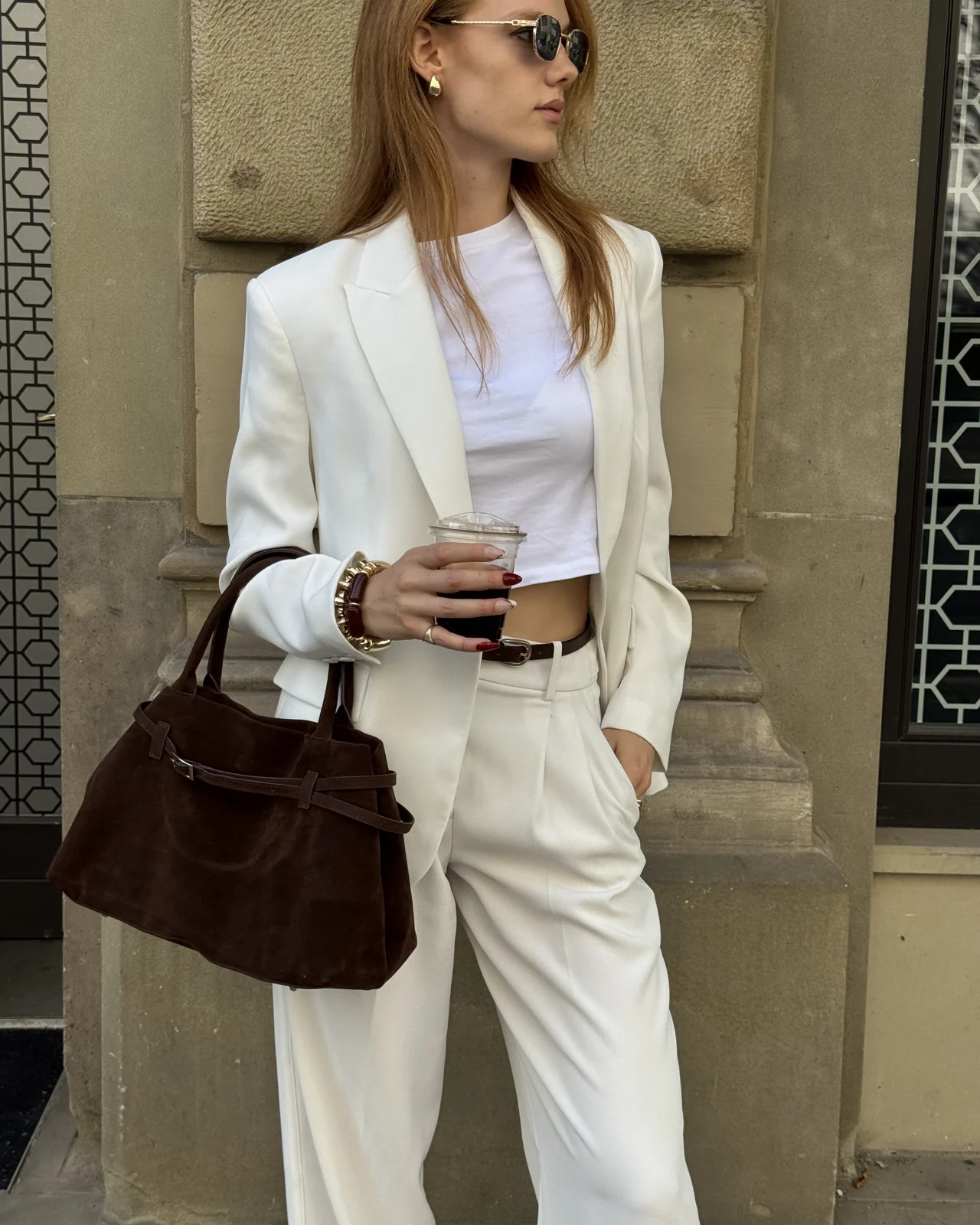 Stella in a white blazer holding a coffee outside